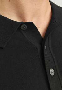 Polo de punto negro con tres botones en el cuello. La textura es suave, con un cuello acanalado y detalles de costura sutiles.
