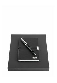 Carnet en cuir noir avec la marque « BOSS » et stylo noir aux accents argentés, posé sur une plateforme carrée noire.