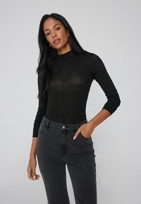 Maglietta nera a maniche lunghe realizzata in tessuto trasparente e texturizzato, abbinata a jeans neri a vita alta. Dettaglio notevole: design aderente con maniche attillate.