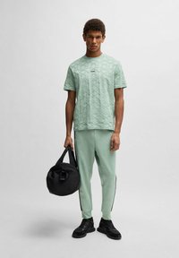Ljus mintgrön texturerad t-shirt med en logotyp, kombinerad med matchande byxor och en svart rund väska. Svarta sneakers fulländar outfiten.