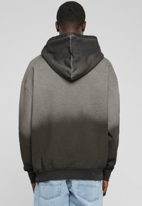 Hanorac cu glugă în nuanțe de gri gradient, cu o textură moale, umeri căzuți și manșete ribbate. Design simplu, potrivit pentru ținute casual.
