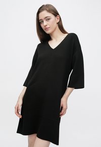 Abito nero lavorato a maglia con scollo a V e maniche a tre quarti, caratterizzato da una vestibilità ampia e un orlo dritto, su sfondo bianco.