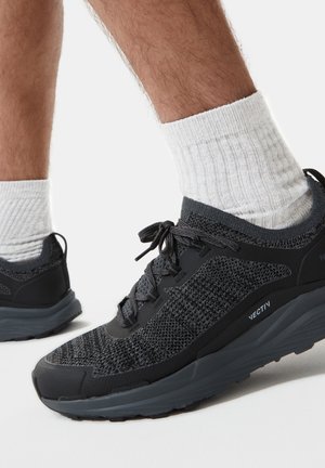 Schwarze Sportschuhe mit strukturierter Strickoberfläche und Gummisohle. Merkmale umfassen ein Schnürdesign und hellgraue Akzente auf der Sohle.