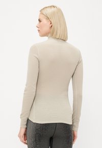 Light beige long-sleeve top with a fitted design, soft texture, and a high neckline. Minimal seam detailing visible on the back.