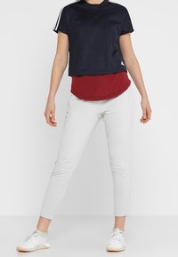 T-shirt cropped blu navy con strisce bianche, indossato su un top rosso. Abbinato a pantaloni bianchi aderenti e sneakers chiare, contribuisce a un look atletico.
