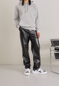 Hoodie grigio tie-dye con tasca frontale, abbinato a pantaloni neri in pelle sintetica con texture a coccodrillo, completato da sneaker bianche.