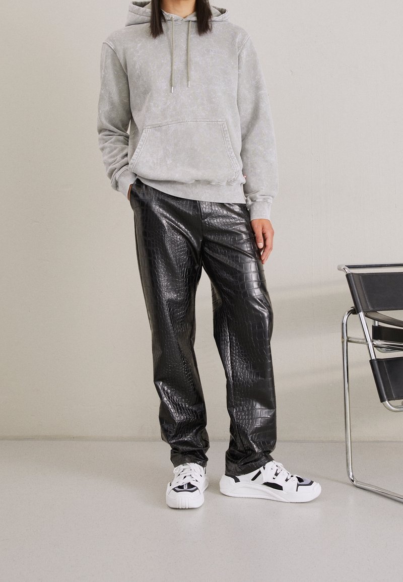 Hoodie grigio tie-dye con tasca frontale, abbinato a pantaloni neri in pelle sintetica con texture a coccodrillo, completato da sneaker bianche.