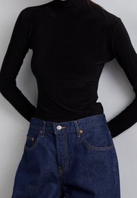 Černý dlouhý rukáv s rolákem v kombinaci s tmavě modrými denimovými džínami. Džíny mají detaily knoflíku a prošití.