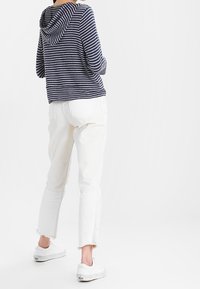 Marinblå randig huvtröja kombinerad med vita slitna jeans och vita sneakers. Inriktning på avslappnad komfort med en lös passform och mjuka texturer.