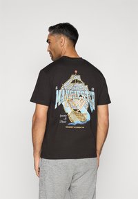 Čierne bavlnené tričko s farebným grafickým dizajnom lode a textom "Manchester City" na zadnej strane. Kolo výstrihu, krátke rukávy.