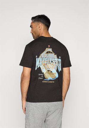 Juodas medvilnės marškinėliai su spalvingu grafiniu laivo dizainu ir užrašu „Manchester City“ nugaroje. Apvalus kaklas, trumpomis rankovėmis.