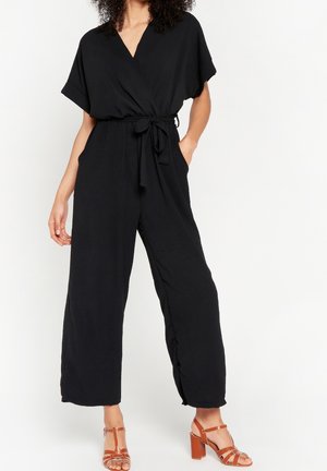 Tuta nera con design a incrocio, maniche corte, vita annodata e pantaloni a gamba larga. Presenta una texture liscia e tasche laterali.