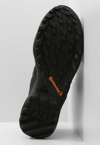 Černá venkovní podrážka boty s texturovaným vzorem pro lepší přilnavost, s oranžovým logem "Continental" a výrazně umístěným emblémem adidas.