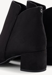 Paire de bottines en daim noir avec talons carrés et un petit détail de logo métallique près du bord supérieur.