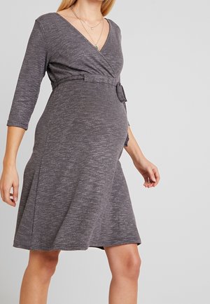 Kobieta w ciąży ubrana w sukienkę kopertową do kolan w kolorze szary melanż, z rękawami do łokcia i materiałowym paskiem w talii.