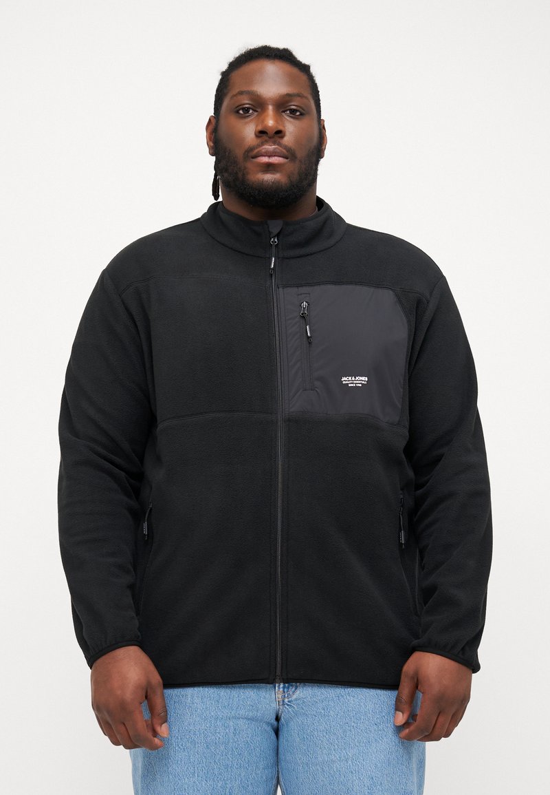 Black fleece jacket with a zippered front, high collar, and a chest pocket featuring black fabric. Two side pockets with zippers.