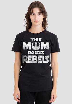 Black cotton t-shirt featuring white text reading "THIS MOM RAISES REBELS" with a symbol. Crew neck and short sleeves, smooth texture.