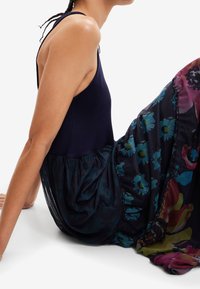 Débardeur côtelé bleu marine associé à une jupe fluide à motifs floraux dans des teintes sombres, ornée d'accents de bleu et de détails multicolores vifs.