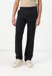 Pantalones negros de corte recto, con un frente plano, passantes para cinturón y una textura suave. Combinados con zapatillas sencillas de color claro.