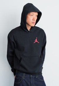 Sort hættetrøje med en frontlomme og et pink Jumpman-logo på brystet, lavet af et blødt og tykt stof.