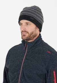 Strikket hat i sort og grå striber med en sort kant. Båret af en model iført en navy fleecejakke med lynlås og røde detaljer.