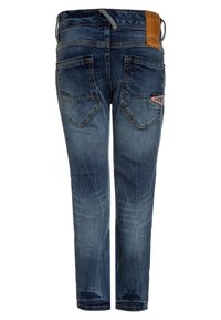 Vista trasera de unos vaqueros de mezclilla azul con un lavado desgastado, dos bolsillos traseros, un parche de cuero marrón de la marca y costuras en contraste.