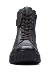Zapatilla alta de cuero negro con superficie texturizada, puntera redonda, cordones planos y suela de goma acanalada. Cuenta con un cierre lateral para facilitar el uso.