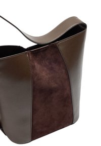 Brązowa skórzana torba na ramię o gładkim wykończeniu, z szerokim otwarciem i centralnym panelem z ciemniejszego zamszu. Zaokrąglone górne krawędzie.