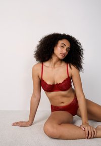 Rode kanten bh en slipset, voorzien van bloemenborduursel, verstelbare banden en doorschijnende panelen. Soepele textuur; gemaakt van nylon en elastaan.