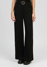 Pantalons larges noirs en tissu doux, avec une taille ajustée et une boucle rond en métal doré sur une ceinture noire. Design élégant et ajusté.