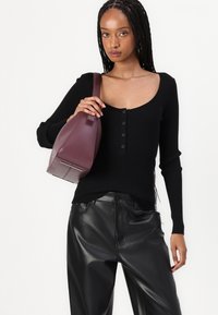 Zwarte geribbelde langemouwen top met een ronde hals en knoopdetails, gecombineerd met zwarte faux leren broek en een bordeaux schoudertas.
