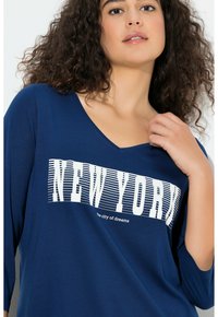 Granatowy, długi rękaw z dekoltem w serek, z białym napisem "NEW YORK" i podtytułem "miasto marzeń" w pogrubionej czcionce szeryfowej. Miękka tkanina.