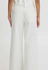 Pantalones anchos de mezclilla blanca. Presentan una cintura alta, dos bolsillos traseros y una textura suave. Sin detalles metálicos visibles.