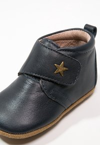 Mörkblå läderbabystövel med kardborreband och en guldig stjärndetalj, med en mjuk insida och en sål av tan mocka.