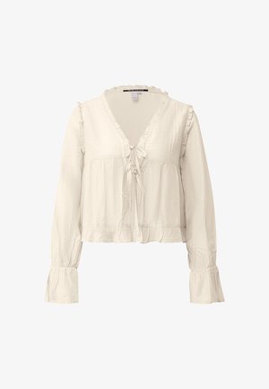 Cream-colored long-sleeve blouse with ruffled edges, front tie closures, and gathered cuffs, made from lightweight fabric.