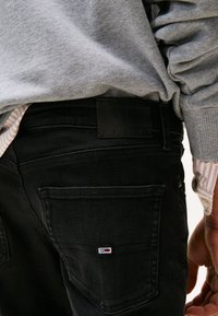 Črne jeans hlače iz jeansa s teksturirano tkanino, vidno logotipno značko in majhno blagovno znamko na zadnjem žepu.