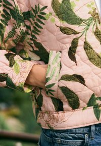 Gestepptes pinkes Jacket mit grünen Blattformen und einem kontrastierenden hellgrünen Bündchen. Der Stoff hat eine weiche Textur und detaillierte Nähte.