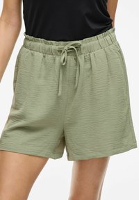 Shorts vert clair en tissu texturé, dotés d'une taille élastique avec cordon de serrage et de poches latérales.