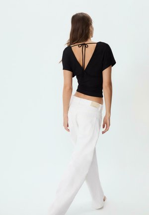 Top nero a maniche corte con schiena a V profonda e dettaglio con fiocco, abbinato a jeans bianchi larghi. Tessuto liscio con una silhouette aderente.
