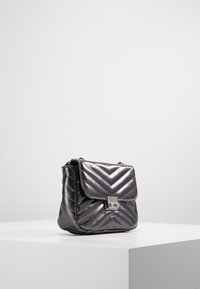 Borsa a tracolla trapuntata di colore grigio metallico con chiusura a pattina e accessori in argento. Presenta un motivo a zig zag e una tracolla a catena. Design compatto.