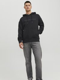 Black hooded sweatshirt with white logo on chest and drawstrings, paired with gray jeans. Fabric appears soft and casual in style.