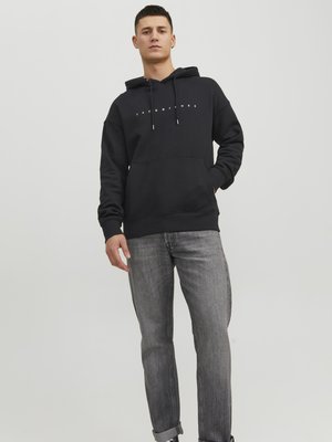Sudadera negra con capucha y logo blanco en el pecho, con cordones, combinada con jeans grises. La tela parece suave y de estilo casual.