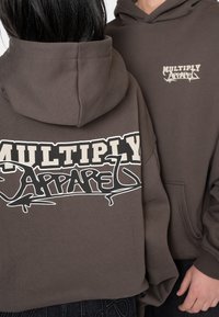 Felpa con cappuccio marrone, caratterizzata da un grande logo grafico bianco e nero sul retro e un logo più piccolo sul lato sinistro del petto.