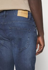 Dark blue denim jeans featuring a leather patch with “ONLY & SONS” logo, back pockets, and a straight fit design.
