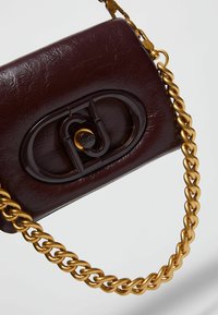 Borsa a mano in pelle bordeaux con finitura lucida, dotata di una tracolla in catena dorata e di un fermaglio rettangolare con dettaglio del logo.