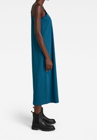 Sirokki väri sleeveless mekko, joka on löysä ja ulottuu polveen. Yhdistetty mustiin nilkkureihin, joissa on elastiset sivupaneelit ja paksu kanta.