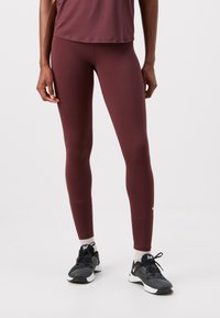 Burgundivörös leggings, rugalmas anyagból, sima textúrával és testhezálló kialakítással. Fekete sportcipővel párosítva.