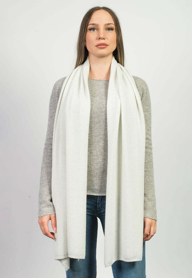 Lang hvid tørklæde lavet af blødt, struktureret materiale, der hænger om halsen, parret med en lys grå sweater og blå jeans.