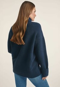 Granatowy wełniany sweter w oversize z wysokim kołnierzem, prążkowanymi mankietami i dołem. Miękka tekstura, luźny krój i boczne rozcięcia dla dodatkowego komfortu.