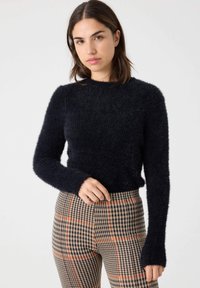 Suéter de felpa azul marino con mangas largas y cuello redondo, acompañado de pantalones de cuadros con tonos negros, marrones y naranjas.